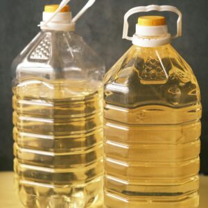 Two large recyclable plastic bottles filled with cooking oil on a yellow surface.